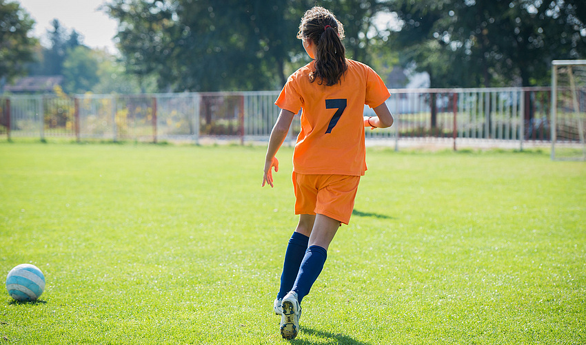 Mädchen im orangefarbenen Trikot auf dem Fußballrasen mit einem Ball