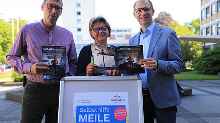 (v.li.n.re.) Prof Dr. Reinhold Merbs (Wetteraukreis, Fachdienst Gesundheit und Gefahrenabwehr), Anette Obleser (Wetteraukreis, Selbsthilfe-Kontaktstelle), Jan Weckler (Landrat des Wetteraukreises), bewerben die 52. Selbsthilfezeitung und die Selbsthilfe-MEILE am 4.07.26 in Bad Nauheim