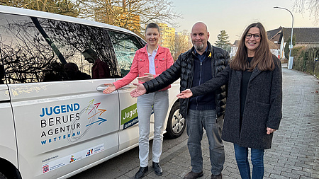 Drei Menschen stehen vor einem Kleinbus.