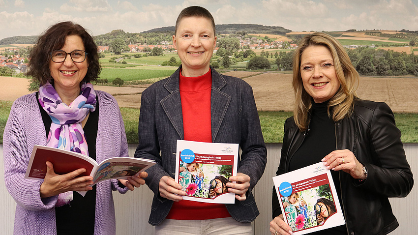 Andrea Rosenberger, Marion Götz und Ann-Karin Schild lächeln in die Kamera. Sie halten Broschüren in der Hand. Im Hintergrund ein Lanschaftsbild