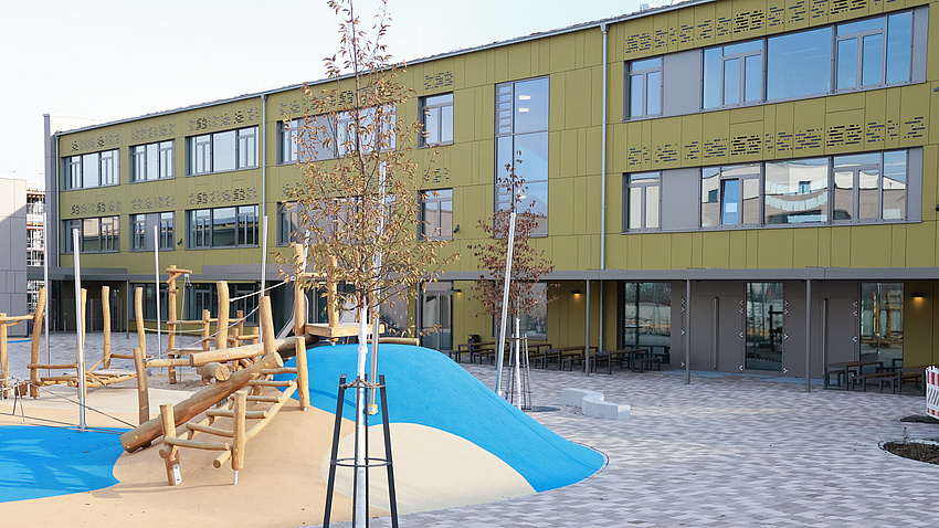 Schulgebäude, davor ein Spielplatz