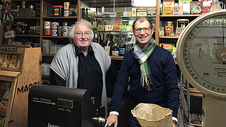 Zwei Männer hinter dem Ladentisch eines historischen Einkaufsladens der Fünfziger Jahre