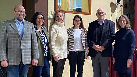 Zwei Männer und vier Frauen stehen vor einem Gebäude.