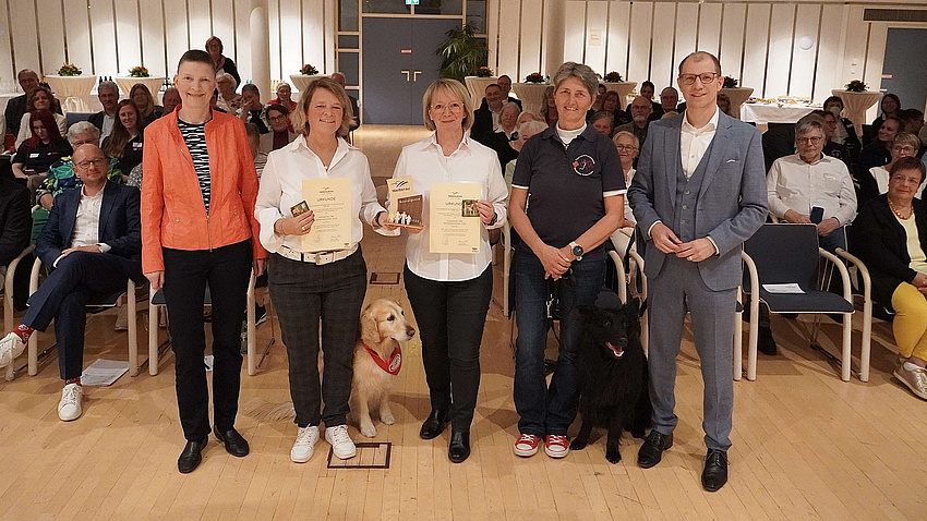 Fünf Personen mit zwei Hunden in einem Saal.