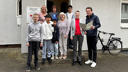 Mehrere Erwachsene und Kinder stehen vor einem Hauseingang und halten einen Zettel in der Hand.