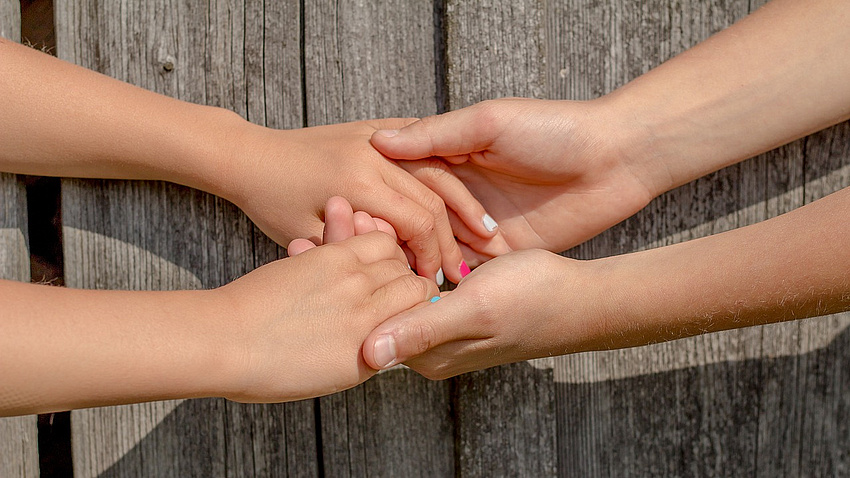 Zwei Paar Hände, die einander halten.