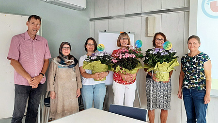Fünf Frauen und ein Mann stehen nebeneinander und blicken lächelnd in die Kamera. Drei der Frauen halten einen Blumenstrauß in der Hand