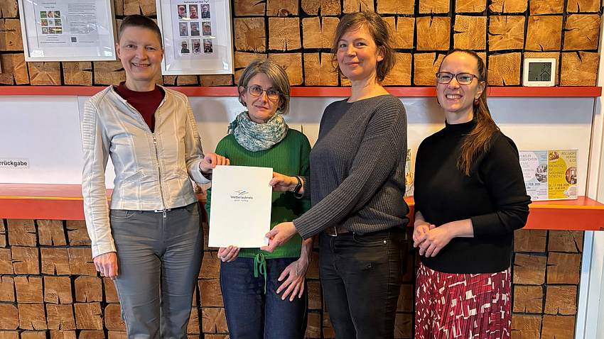 Vier Frauen halten eine Dokument in die Kamera.