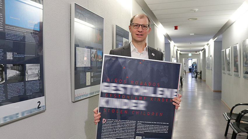 Landrat Jan Weckler steht mit einem Bilderrahmen in den Händen in einem langen Flur.
