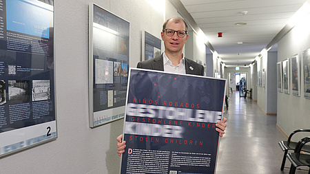 Landrat Jan Weckler steht mit einem Bilderrahmen in den Händen in einem langen Flur.