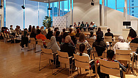 Ein großer Raum, auf der Bühne sitzen fünf Frauen, davor ca. 50 Frauen im Publikum