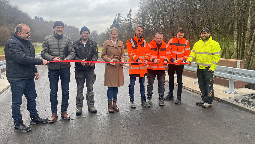 Sieben Personen auf einer Straße. Sie schneiden ein rotes Band durch.