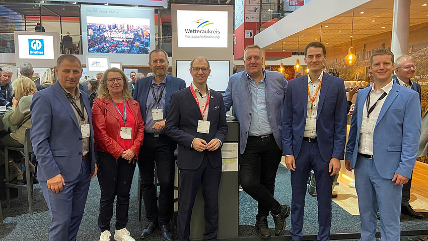 Sieben Personen stehen vor einem Bildschirm mit der Aufschrift Wetteraukreis