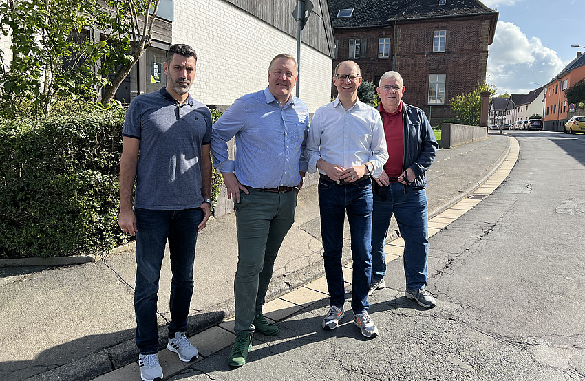 Vier Männer stehen am Straßenrand vor dem Gehweg.