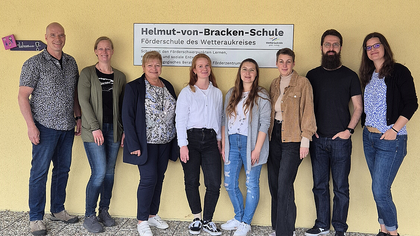 Acht Menschen stehen vor einem Schild, auf dem Helmut-von-Bracken-Schule steht.