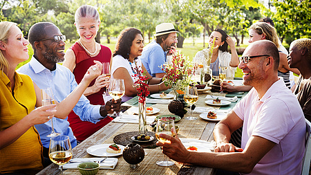 Eine Gruppe Menschen sitzen lächelnd am Tisch. Sie essen und trinken gemeinsam.