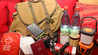 Das Bild zeigt einen Rucksack, haltbare Lebensmittel, Medikamente und die wichtigsten persönlichen Dokumente wie den Reisepass.