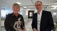 Zwei Menschen stehen vor Vitrinen und halten ein Kunstwerk in der Hand.