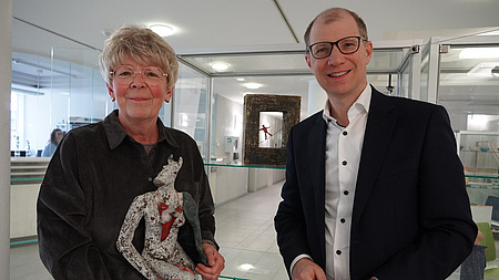 Zwei Menschen stehen vor Vitrinen und halten ein Kunstwerk in der Hand.