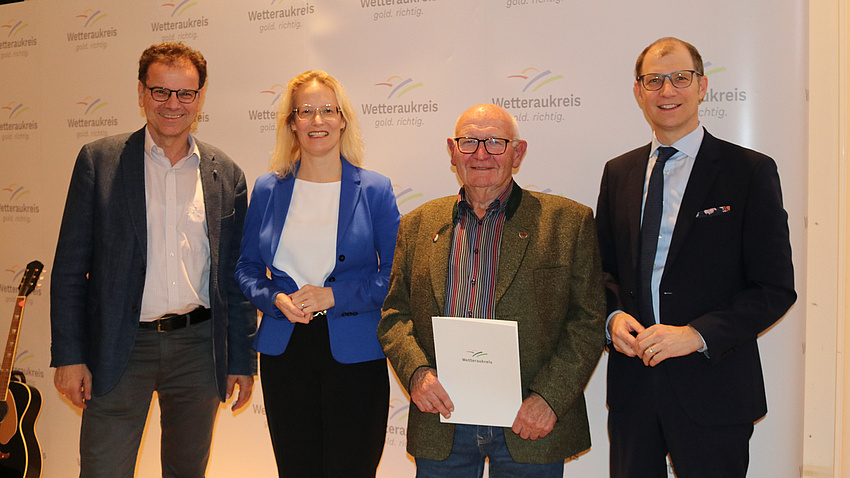 Auf dem Bild sind vier Personen zur sehen. Sie feiern die Verleihung des Umweltschutzpreises des Wetteraukreises, der Empfänger der Belobigung hält hält ihre Urkunde in der Hand.