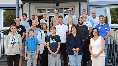 Eine größere Personengruppe steht auf einer Treppe vor dem Eingang eines Gebäudes.