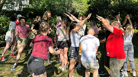 Eine Gruppe von jungen Erwachsenen spielt ein Bewegungsspiel auf einer Wiese.