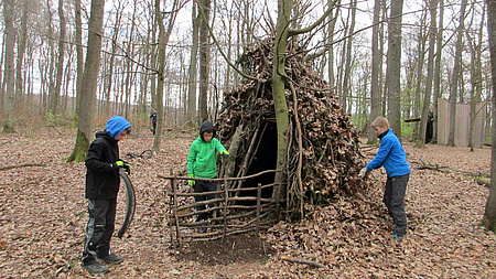 Dre Jungen bauen mit Hölzern und Blättern eine Hütte