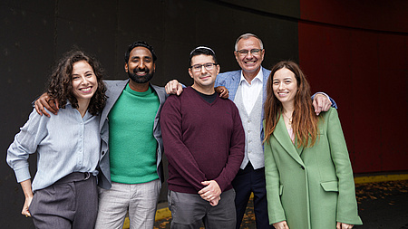 Eine Gruppe von Männern und Frauen lächelt in die Kamera. Der Mann in der Mitte hat eine Kippa auf.