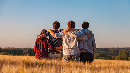 4 Personen von hinten stehen in einer Reihe im Kornfeld und halten sich in den Armen