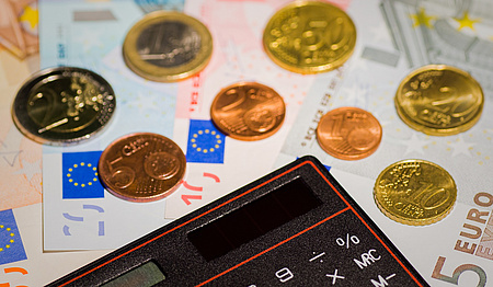 Ein Taschenrechner, daneben Münzen, die auf Geldscheinen liegen.
