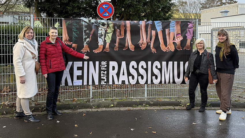 Vier Frauen stehen vor einem Plakat mit der Aufschrift "Kein Platz für Rassismus".