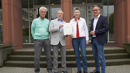 Vier Personen stehen zur Übergabe eines Bewilligungsbescheids vor dem Kreishaus des Friedberger Europaplatzes.