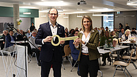 Zwei Personen, Landrat uns Schulleiterin, stehen nebeneinander und halten einen großen goldenen Schlüssel fest, der symbolisch bei der Einweihung der neuen Quellenschule übergeben wird.