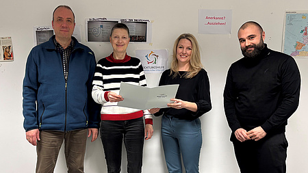 Marion Götz übergibt ein Dokument an Kathrin Anders-Hoffmann, Minas Mandt und Alexander Schanz.