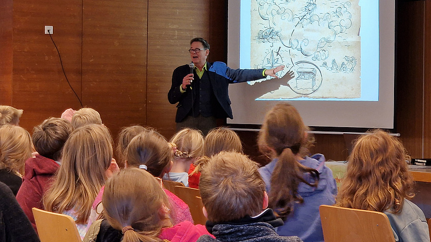 Der Kinderbuchautor Kai Pannen steht vor einer Schulklasse.