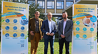 Prof. Dr. Reinhold Merbs, Landrat Jan Weckler und Dr. Alexander Jakob stehen auf einer Wiese. Neben ihnen zwei Roll-Ups zum Thema Hitzeschutz.
