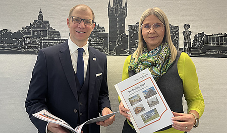 Die beiden halten den Schulbaubericht in der Hand.