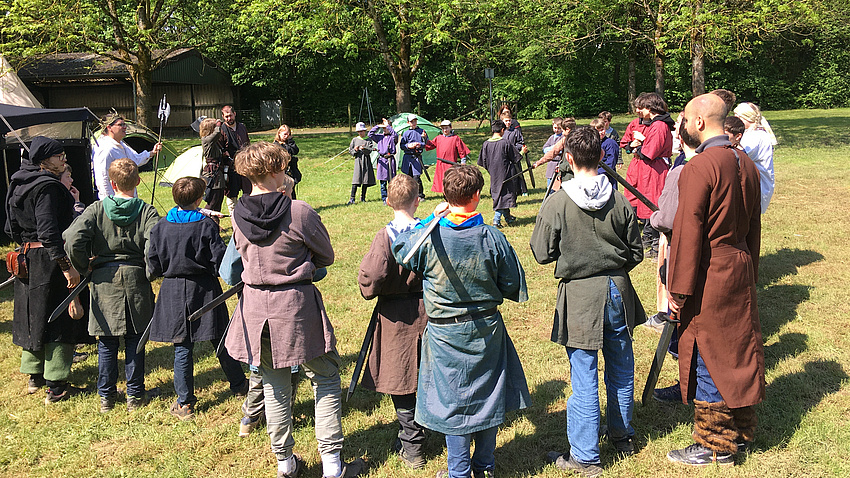 Jugendliche in mittelalterlicher Gewandung stehen in einem Kreis.