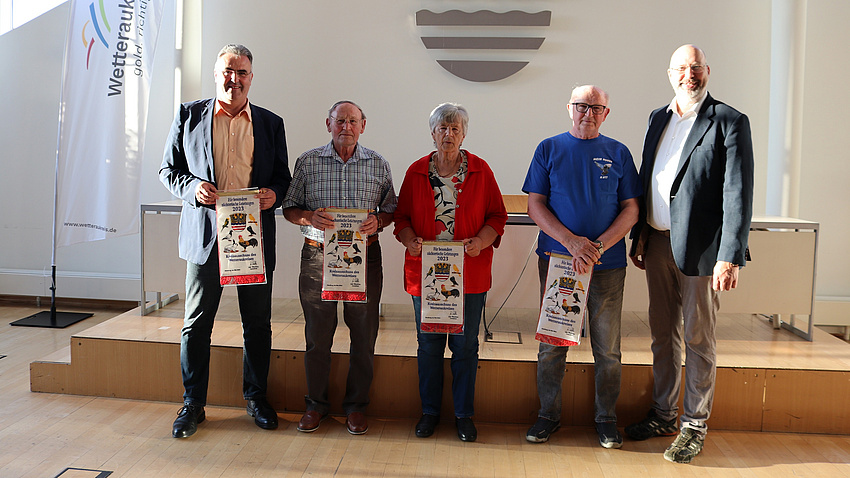 Mehrere Menschen stehen in einem Saal und halten Urkunden in den Händen.