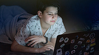 Ein Junge liegt in einem abgedunkelten Raum und schaut sich etwas auf einem Laptop an