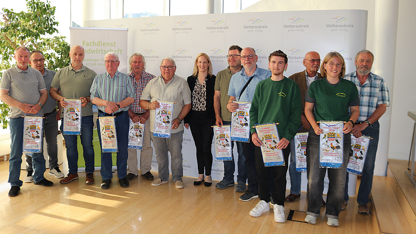Zahlreiche Frauen und Männer stehen mit Wimpeln in der Hand vor einer Stellwand.