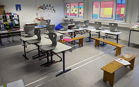 Ein Klassenzimmer. Die Tische sind in der Form eines U gestellt, darauf sind Stühle zu sehen.
