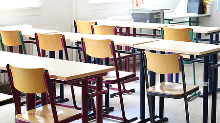 In einem Klassenraum stehen mehrere Tische und Stühle in säuberlichen Reihen.