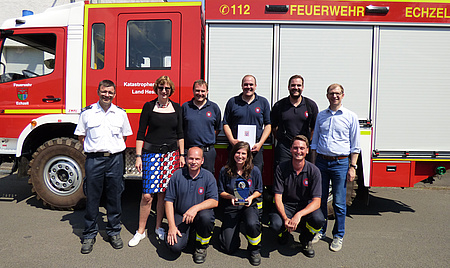 Eine Gruppe Männer und Frauen steht vor einem Löschfahrzeug der Freiwilligen Feuerwehr Echzell.