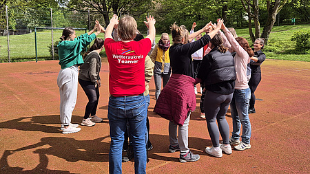 Mehrere Jugendliche stehen auf einem Sportplatz in einem Kreis.
