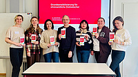 Eine Gruppe von Leuten. Sie halten ein Dokument in der Hand und lächeln.