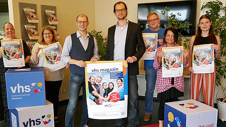 Die Damen und Herren machen einen Foto vor VHS-Würfeln.