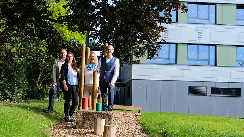 Zwei Männer und zwei Frauen stehen vor einem modernen Schulgebäude.