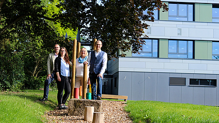 Zwei Männer und zwei Frauen stehen vor einem modernen Schulgebäude.