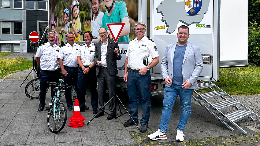 Eine Gruppe von Leuten steht vor einem Lastwagen. Um sie herum sind Verkehrsschilder, ein Fahrrad und Verkehrskegel drapiert.